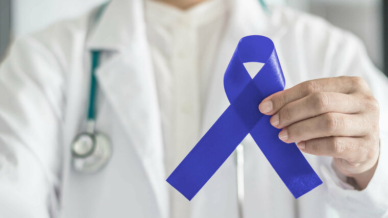 Arzt hält blaue Schleife als Symbol für Darmkrebs in die Kamera