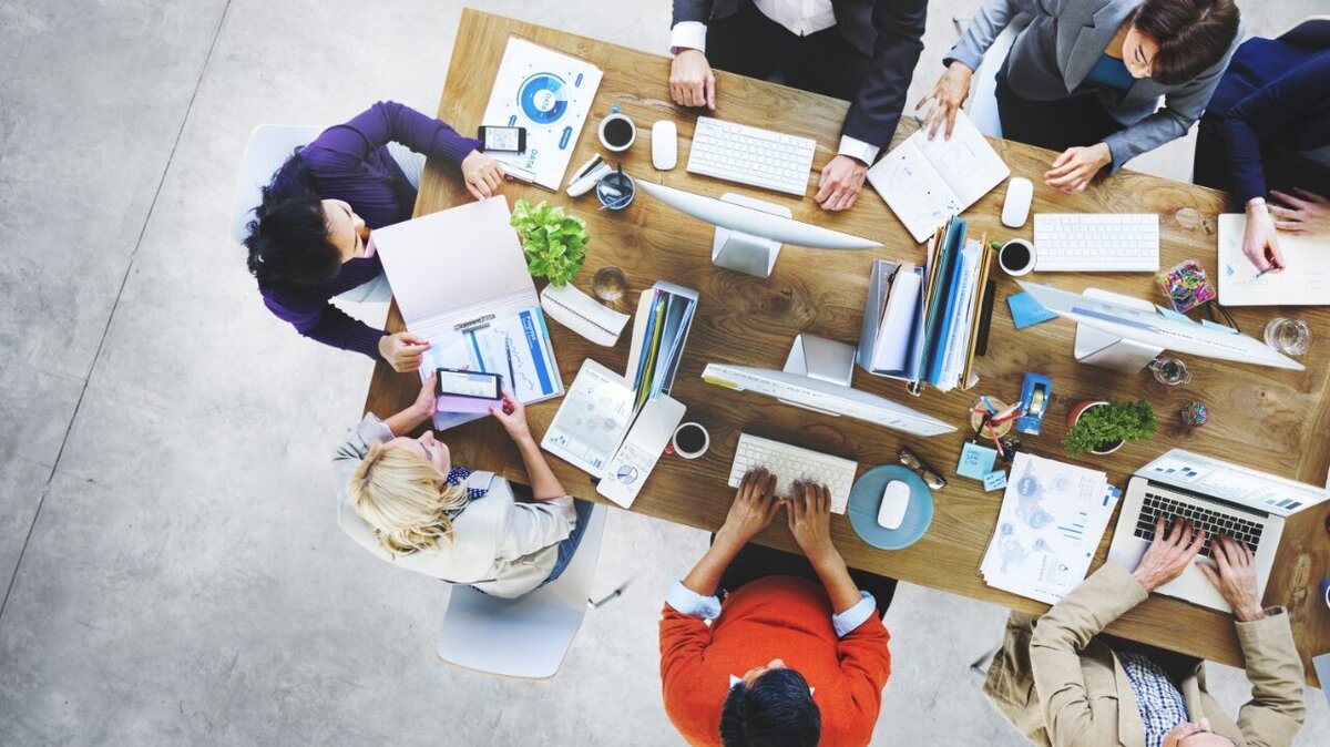 Ein großer Arbeitstisch mit mehreren arbeitenden Menschen daran von Oben