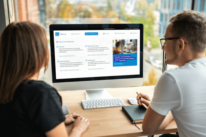 Ein Mann und eine Frau schauen auf einen Monitor mit einer Oberfläche aus dem "Mein ias"-Portal