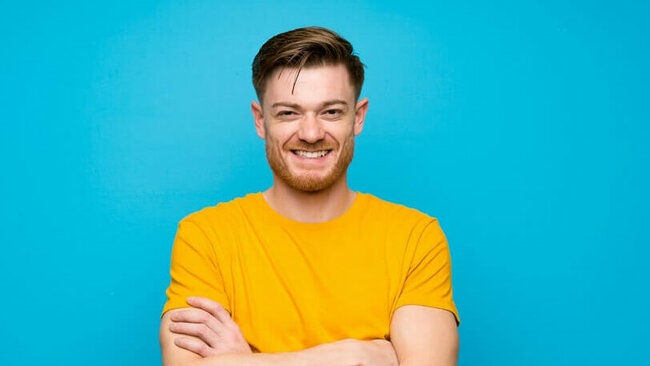 lächelnder junger Mann, gelbes Shirt, blauer Hintergrund