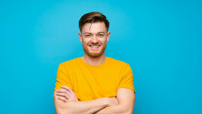 lächelnder junger Mann, gelbes Shirt, blauer Hintergrund