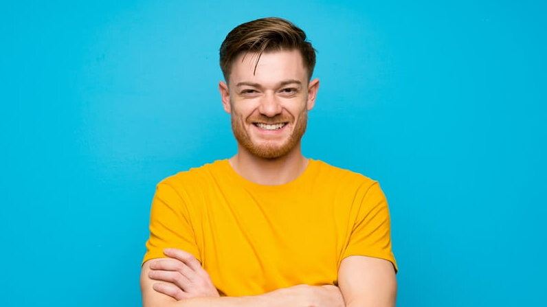 lächelnder junger Mann, gelbes Shirt, blauer Hintergrund