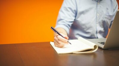 junger Mann am Laptop macht sich schriftliche Notizen