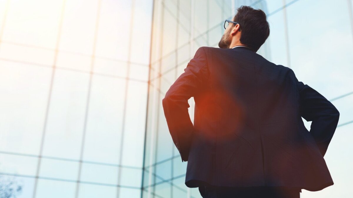 Eine Führungskraft steht mit dem Rücken zugewendet und blickt zu einem Gebäude hinauf.