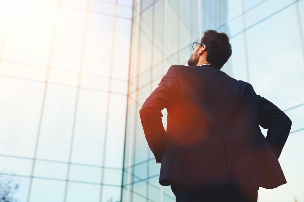 Eine Führungskraft steht mit dem Rücken zugewendet und blickt zu einem Gebäude hinauf.