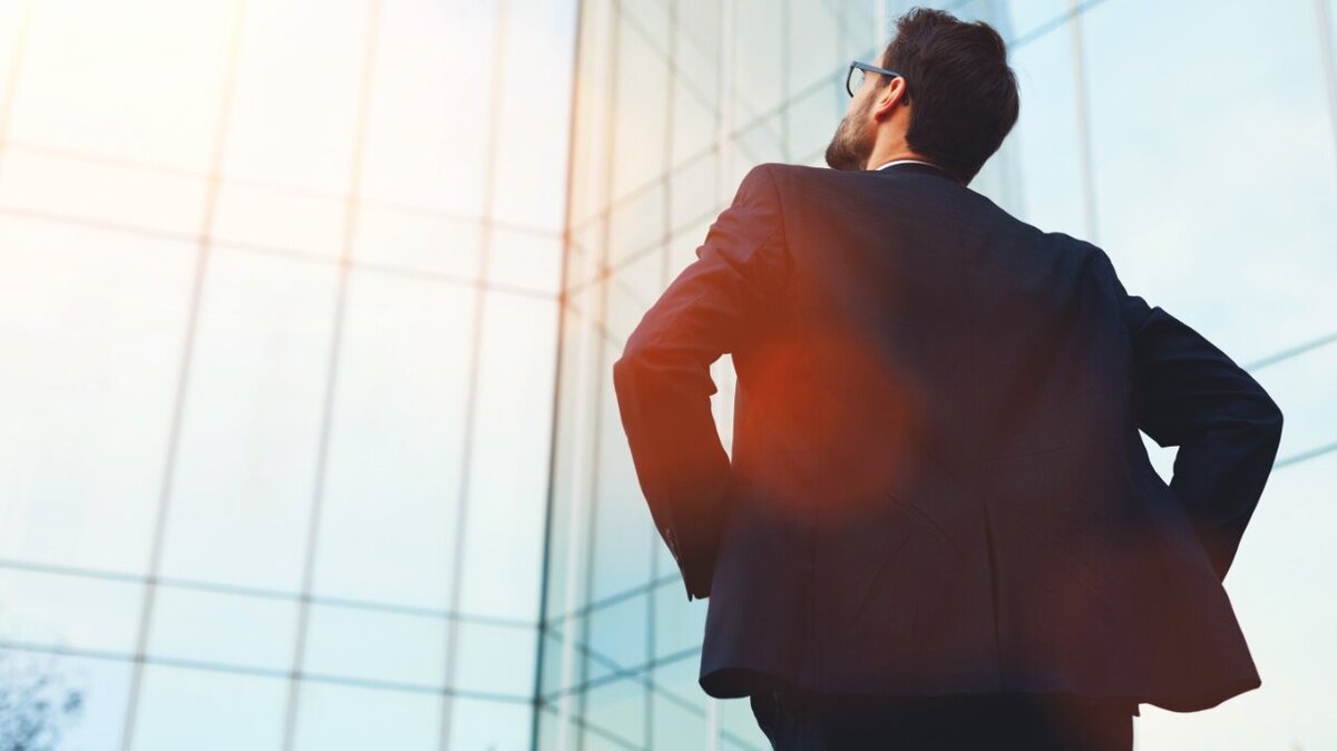 Eine Führungskraft steht mit dem Rücken zugewendet und blickt zu einem Gebäude hinauf.