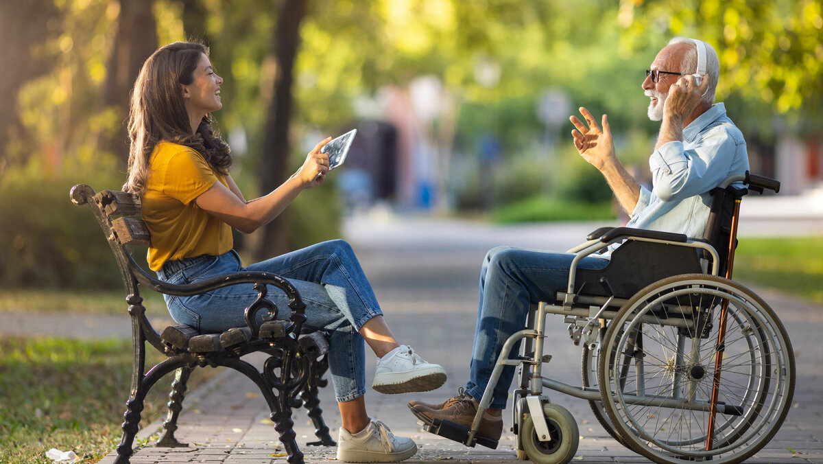 Ältere Mann im Rollstuhl sitzt mit junger Frau im Park