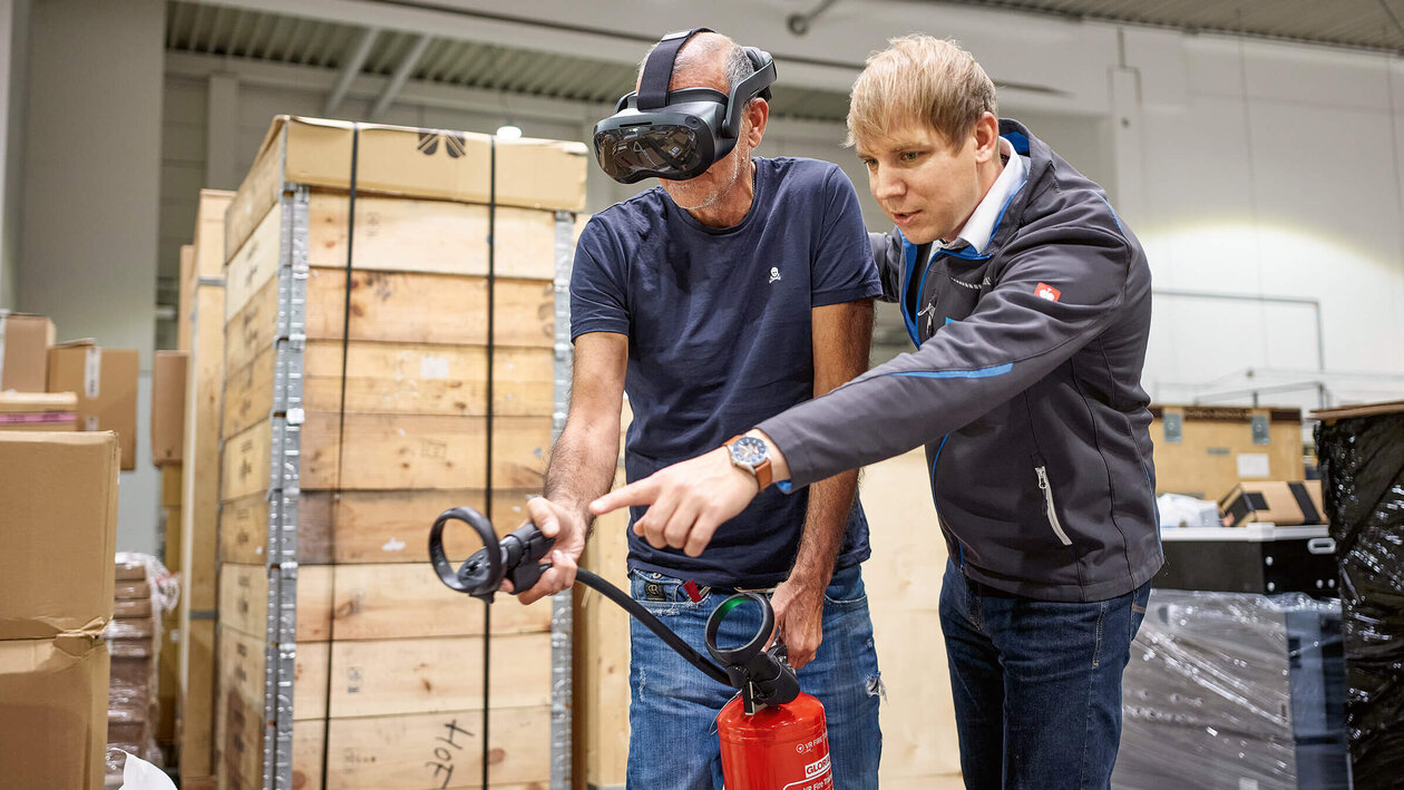 Brandschutz mit VR-Brille Konica Minolta Brandschutzausbildung mit Virtuell Reality, zwei Personen üben mit einem Feuerlöscher einen simulierten Brand zu löschen