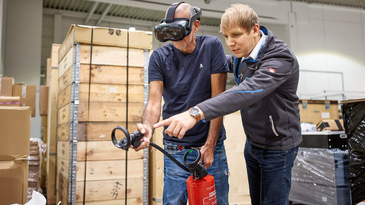 Brandschutz mit VR-Brille Konica Minolta Brandschutzausbildung mit Virtuell Reality, zwei Personen üben mit einem Feuerlöscher einen simulierten Brand zu löschen