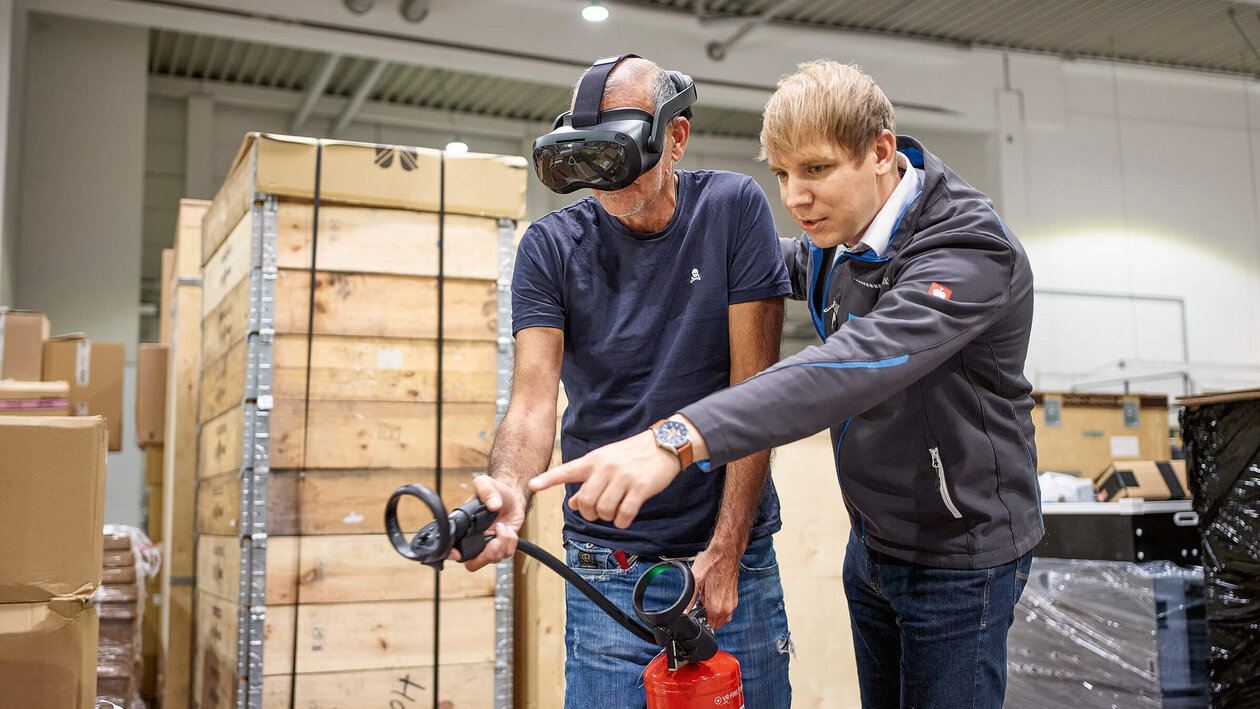 Brandschutz mit VR-Brille Konica Minolta Brandschutzausbildung mit Virtuell Reality, zwei Personen üben mit einem Feuerlöscher einen simulierten Brand zu löschen