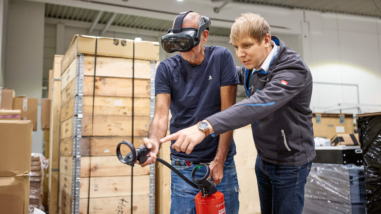 Brandschutz mit VR-Brille Konica Minolta Brandschutzausbildung mit Virtuell Reality, zwei Personen üben mit einem Feuerlöscher einen simulierten Brand zu löschen