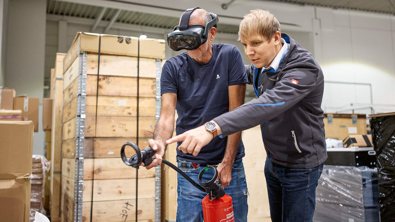 Brandschutz mit VR-Brille Konica Minolta Brandschutzausbildung mit Virtuell Reality, zwei Personen üben mit einem Feuerlöscher einen simulierten Brand zu löschen