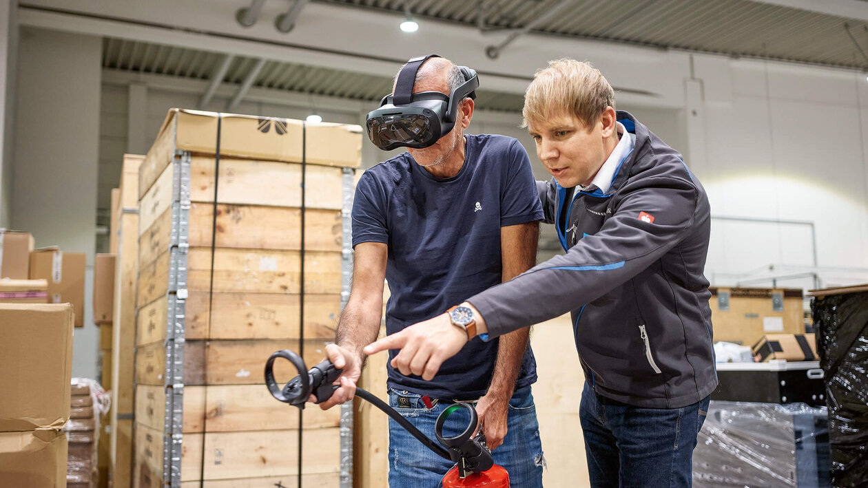 Brandschutz mit VR-Brille Konica Minolta Brandschutzausbildung mit Virtuell Reality, zwei Personen üben mit einem Feuerlöscher einen simulierten Brand zu löschen