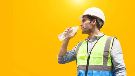 Mann mit Helm und Arbeitsweste trinkt aus einer Flasche