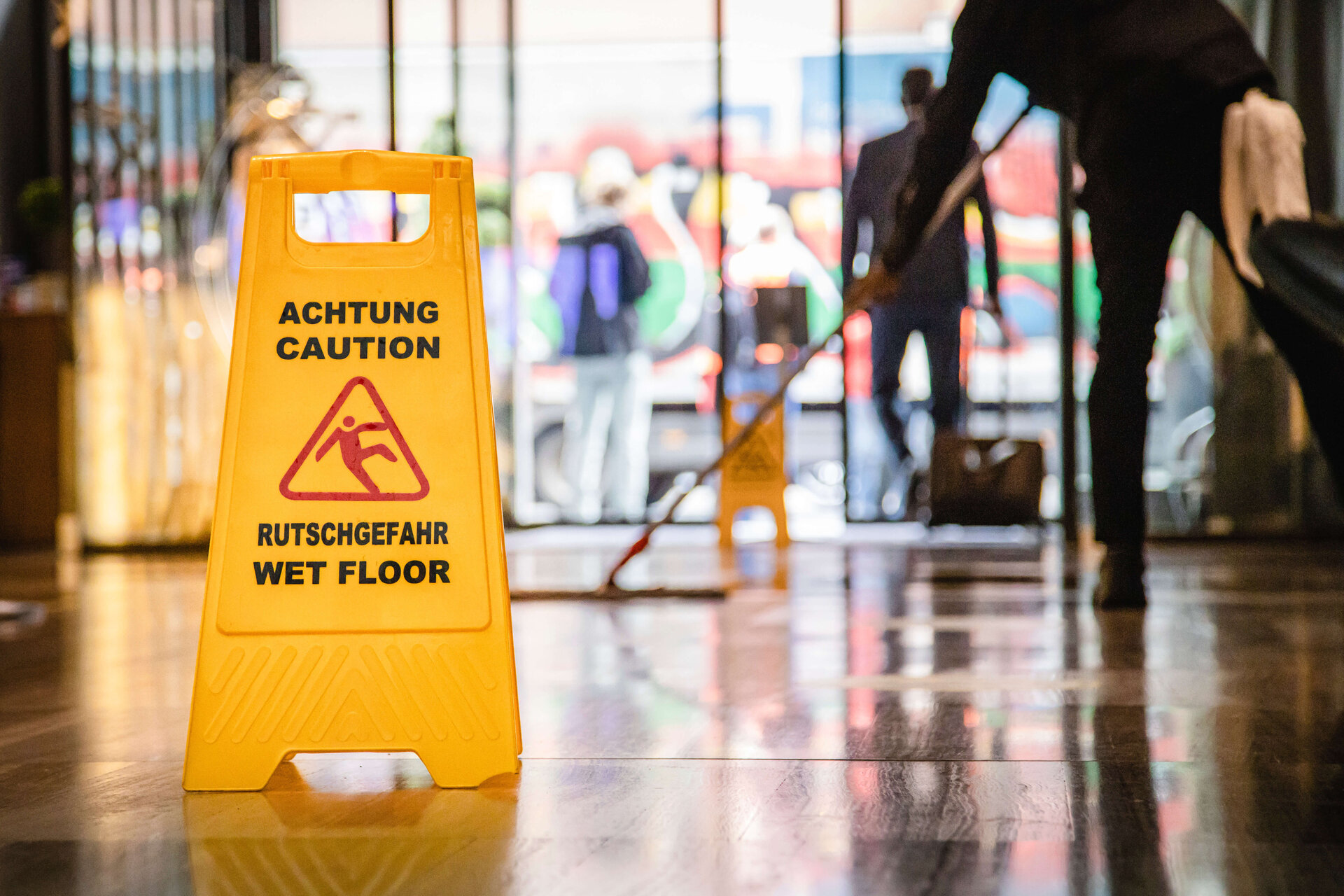 Putzkraft bei der Arbeit, Schild zu Rutschgefahr auf dem Boden