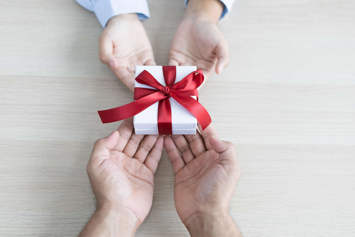 Corporate Benefits als Geschenk überreichen Zwei Hände überreichen ein Geschenk mit roter Schleife an andere zwei Hände