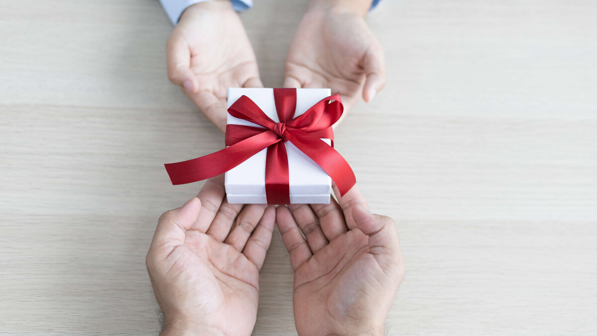 Corporate Benefits als Geschenk überreichen Zwei Hände überreichen ein Geschenk mit roter Schleife an andere zwei Hände