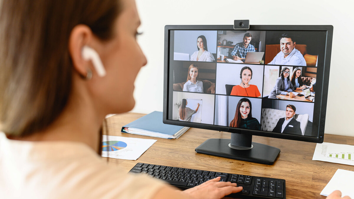 A woman connects with many employees via video looking at webcam