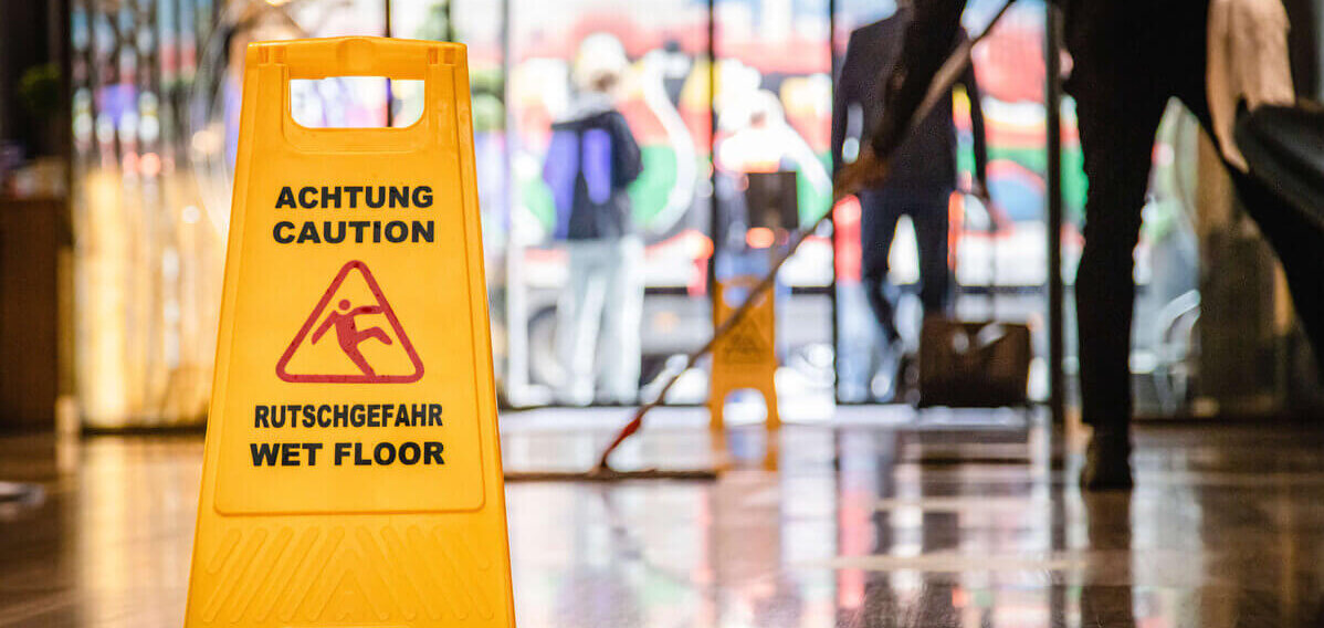 Putzkraft bei der Arbeit, Schild zu Rutschgefahr auf dem Boden