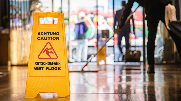 Putzkraft bei der Arbeit, Schild zu Rutschgefahr auf dem Boden