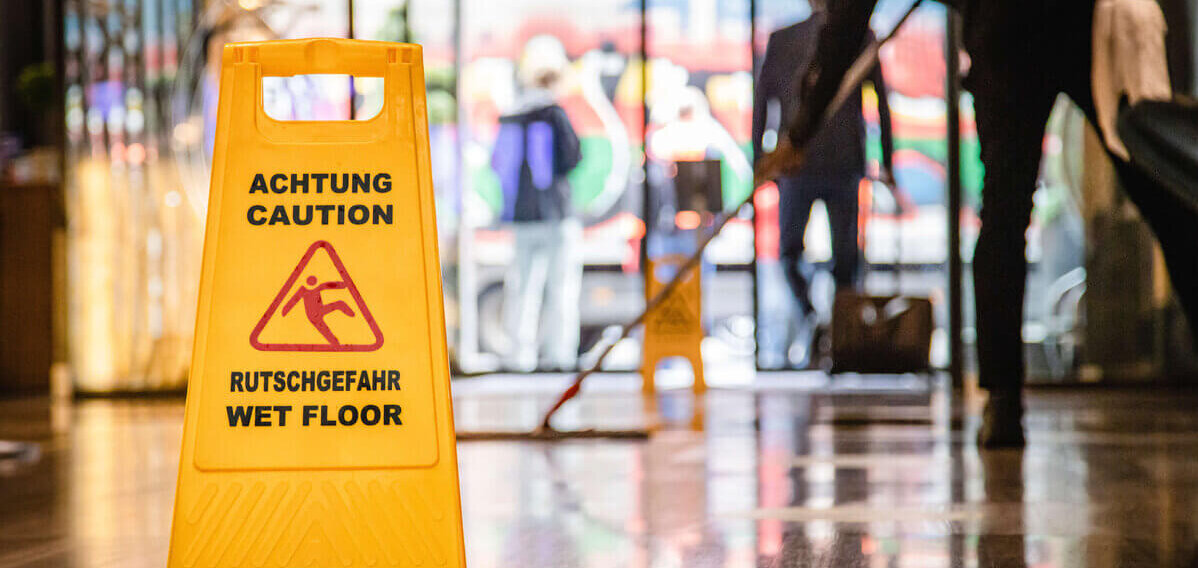 Putzkraft bei der Arbeit, Schild zu Rutschgefahr auf dem Boden