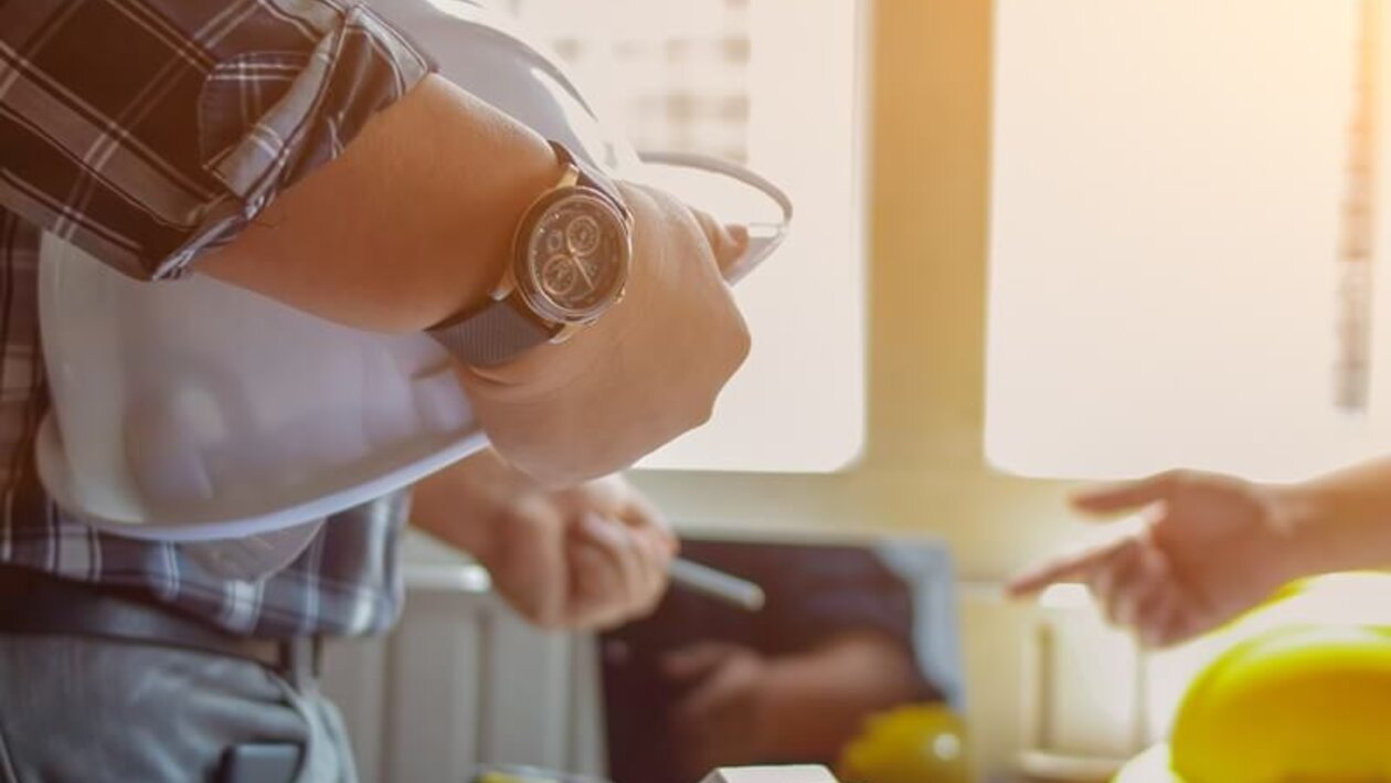 Mann im Karohemd mit weißem Sicherheitshelm unter dem Arm