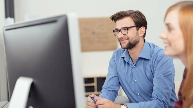 Mann und Frau schauen lächelnd auf einen PC-Bildschirm