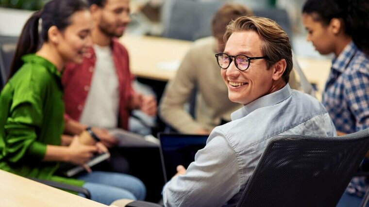 lächelnder Mann mit Brille sitzend in einer Runde mit Kolleg:innen