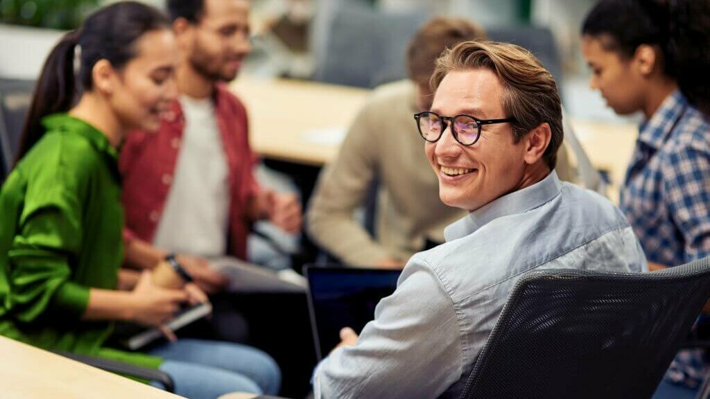 lächelnder Mann mit Brille sitzend in einer Runde mit Kolleg:innen