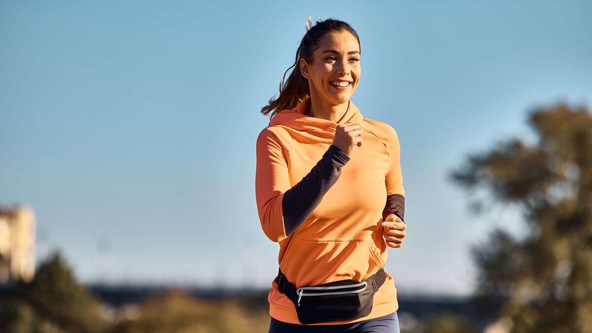 Frau die lächelnd in einem orangenen Pullover joggt 