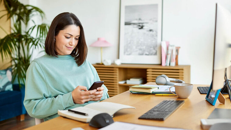 Frau sitzt am Arbeitsplatz und prüft ihr Handy