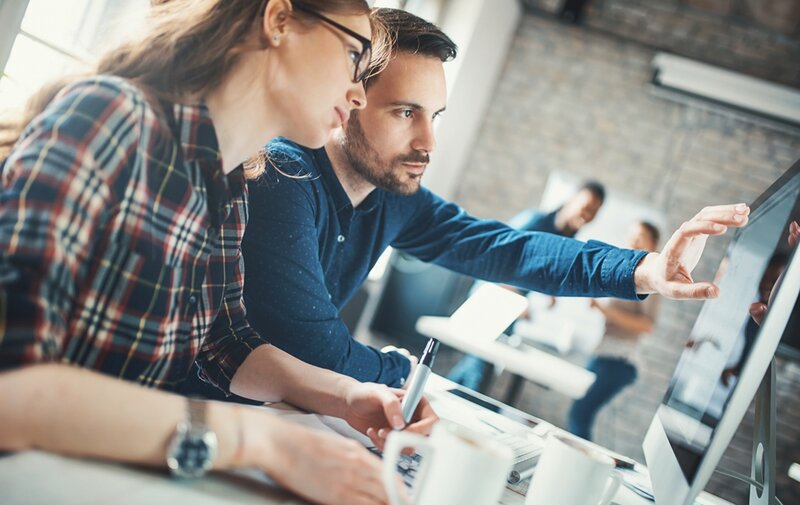 Zwei Kollegen besprechen sich am Arbeitsplatz am Monitor