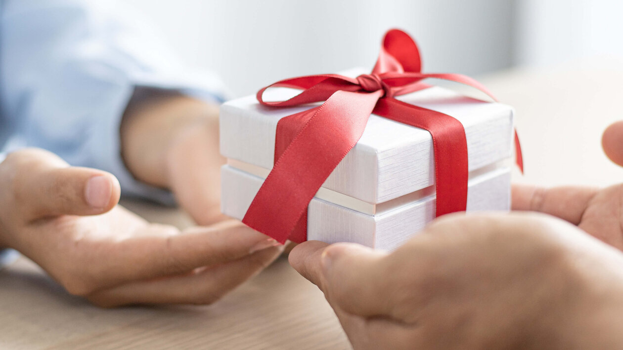Corporate Benefits als Geschenk überreichen Zwei Hände überreichen ein Geschenk mit roter Schleife an andere zwei Hände