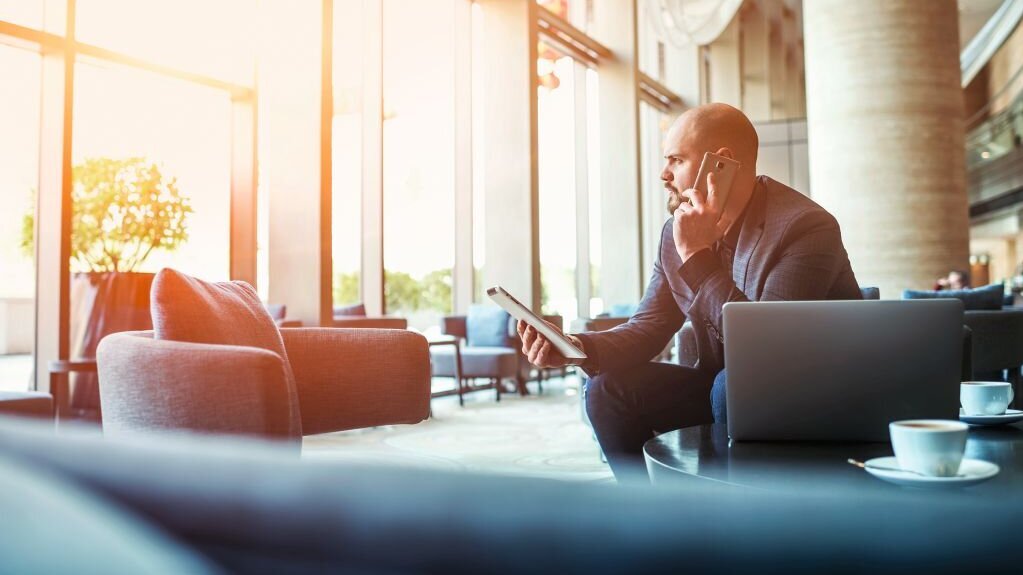 Ein Mann sitzt am Computer, hält ein Tablet in der Hand und telefoniert