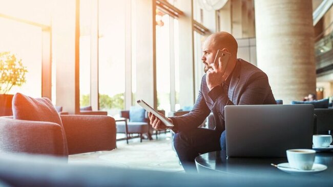 Ein Mann sitzt am Computer, hält ein Tablet in der Hand und telefoniert