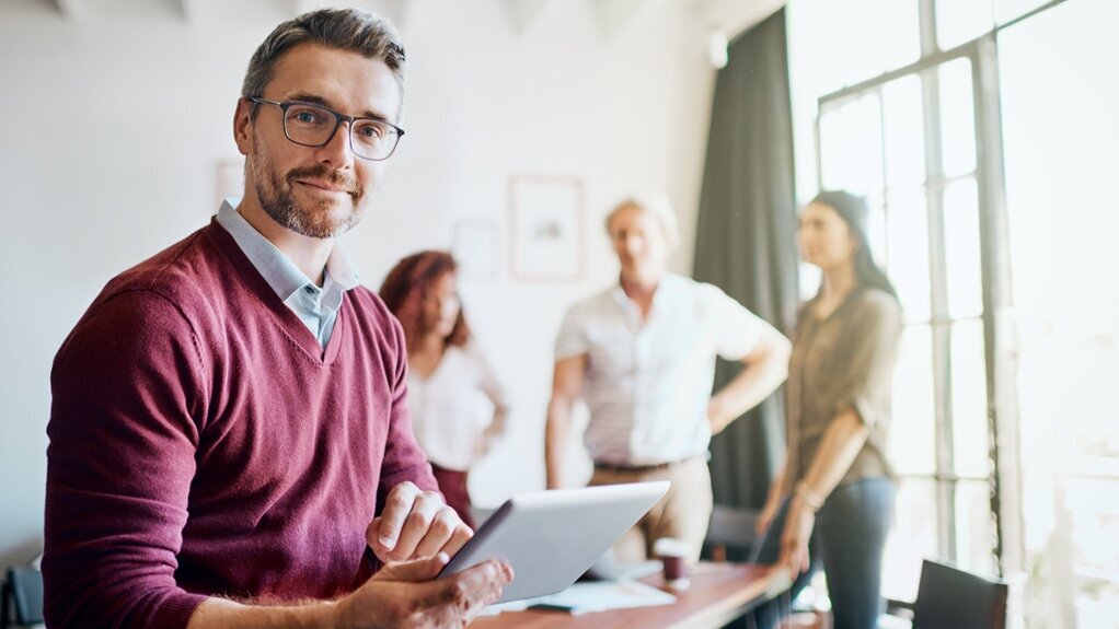 Portrait eines sympatisch lächelnden Teamleader im bordeaux-farbenen Pullover