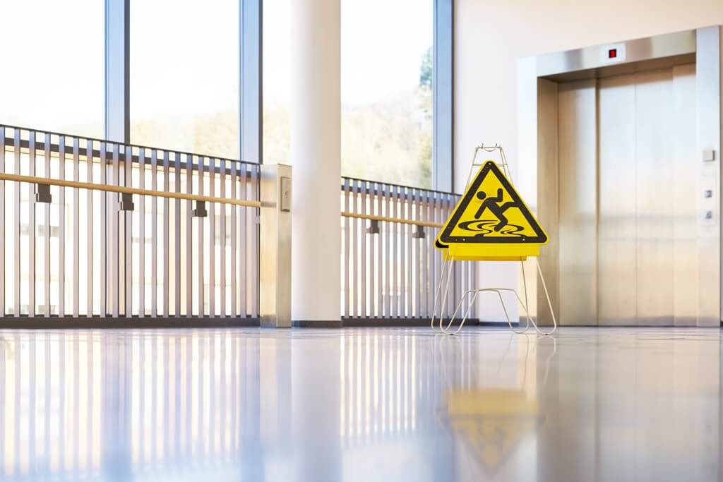 Gefährdungsbeurteilung - Zentrales Element im Arbeitsschutz Warnschild zur Rutschgefahr in einem Flurweg zum Fahrstuhl
