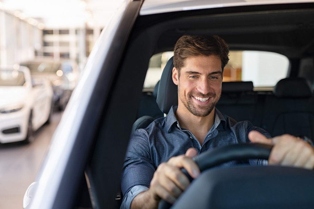 lächelnder Mann im Jeanshemd sitzt in Auto hinter dem Steuer